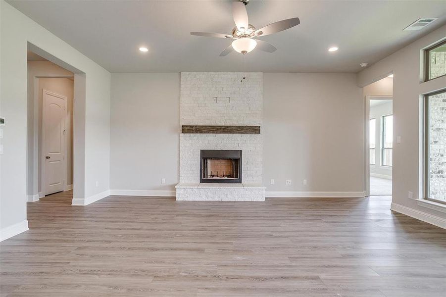 Unfurnished living room with a fireplace, light wood-type flooring, and ceiling fan