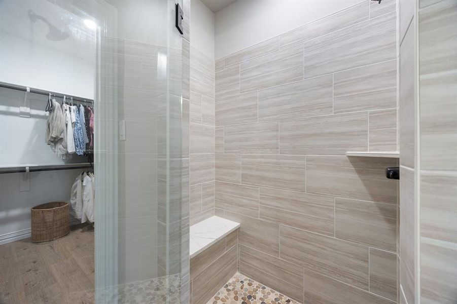 Full bath with a spacious closet, tiled shower, and wood finished floors