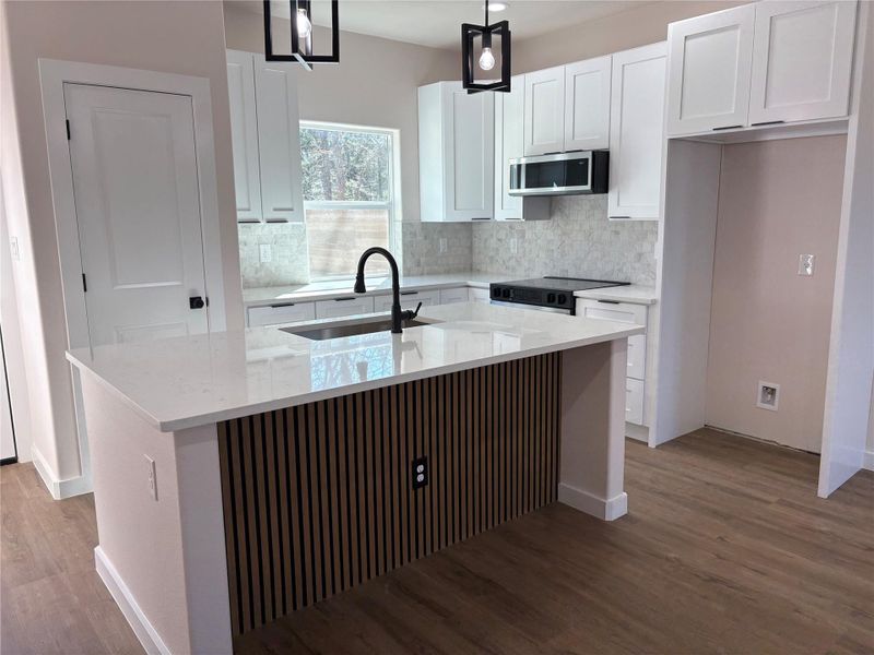 Kitchen with light stone countertops, white cabinets, an island with sink, light wood-style flooring, and stainless steel microwave