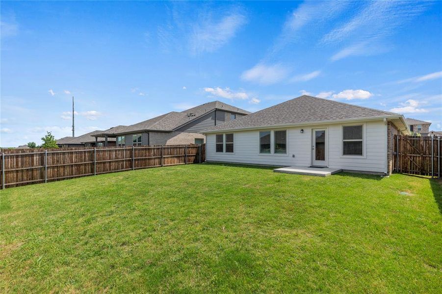 Expansive fenced backyard featuring a grassy lawn, white siding, and a back door with an adjacent concrete pad