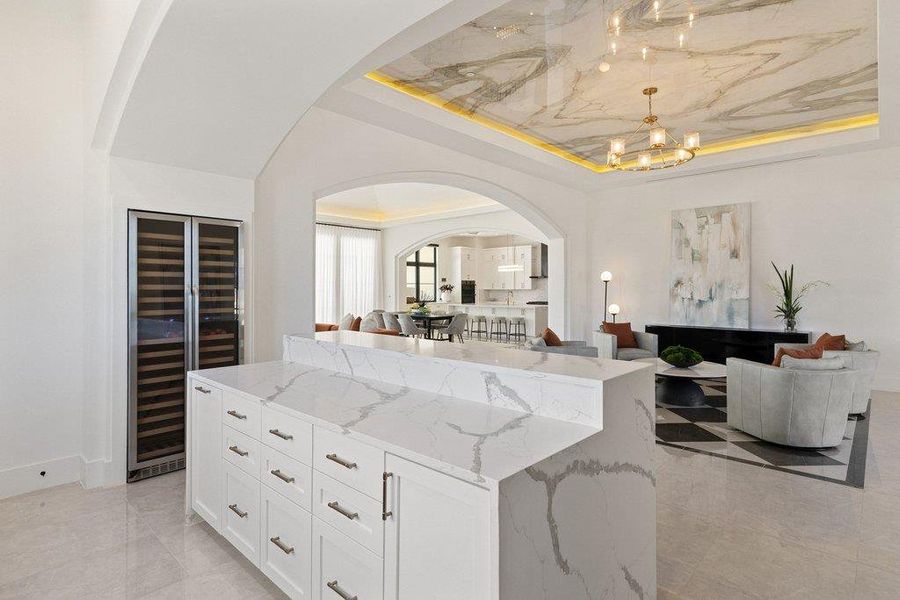 A grand, open-concept living area features a kitchen island, wine cooler, and high ceilings with marble-look detailing.
