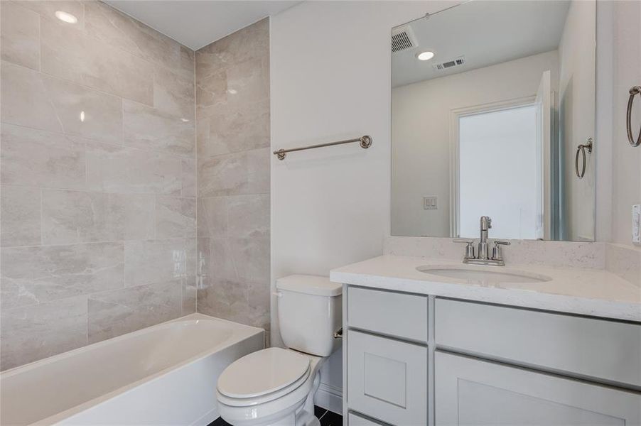 Full bathroom with tiled shower / bath, vanity, and toilet