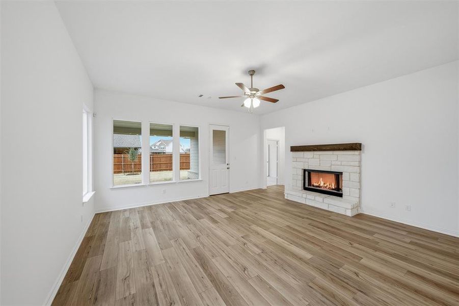 Unfurnished living room featuring light wood-type flooring, a stone fireplace, and a ceiling fan