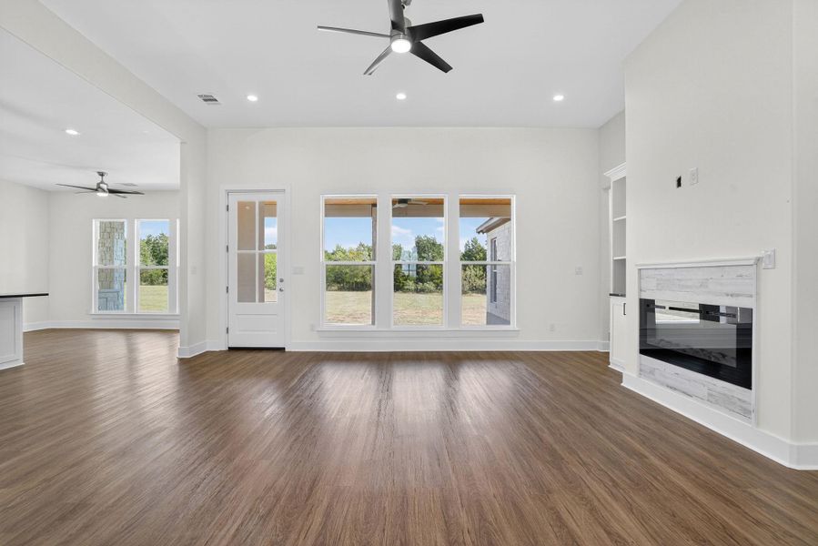 Unfurnished living room featuring a ceiling fan, dark wood-style flooring, recessed lighting, a glass covered fireplace, and built in features Unfurnished living room featuring a ceiling fan, dark wood-style flooring, recessed lighting, a glass covered fireplace, and built in features