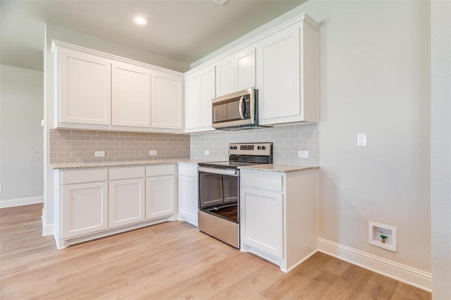 Kitchen featuring light hardwood / wood-style flooring, backsplash, stainless steel appliances, light stone counters, and white cabinets