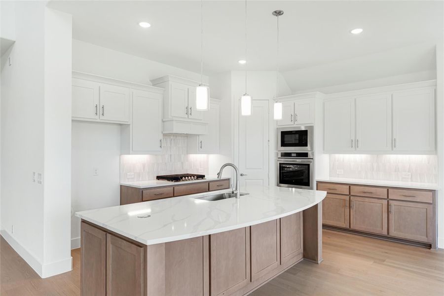 Kitchen with large curved island, white quartz countertops, white upper cabinets, wood lower cabinets, and stainless steel double ovens
