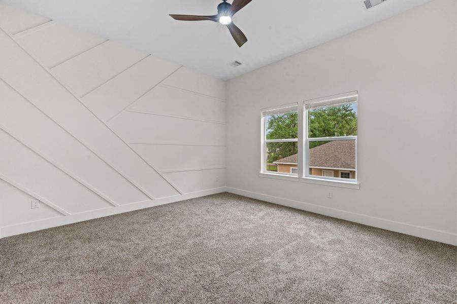 Spacious bedroom featuring a stylish accent wall, plush carpeting, and ample natural light from dual windows.