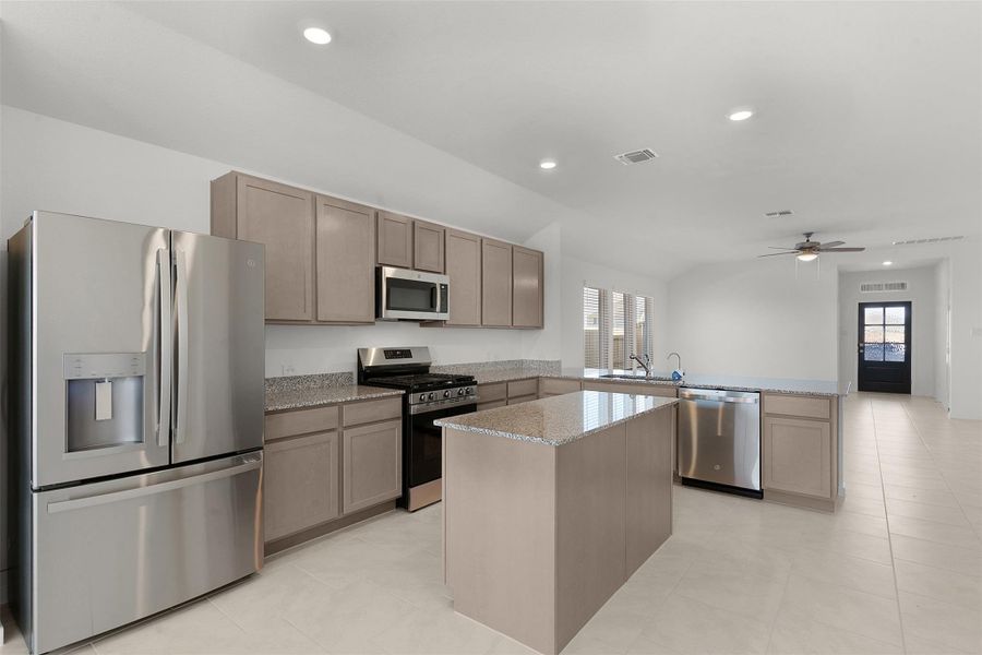 Kitchen with stainless steel appliances, a peninsula, a center island, light stone countertops, and recessed lighting