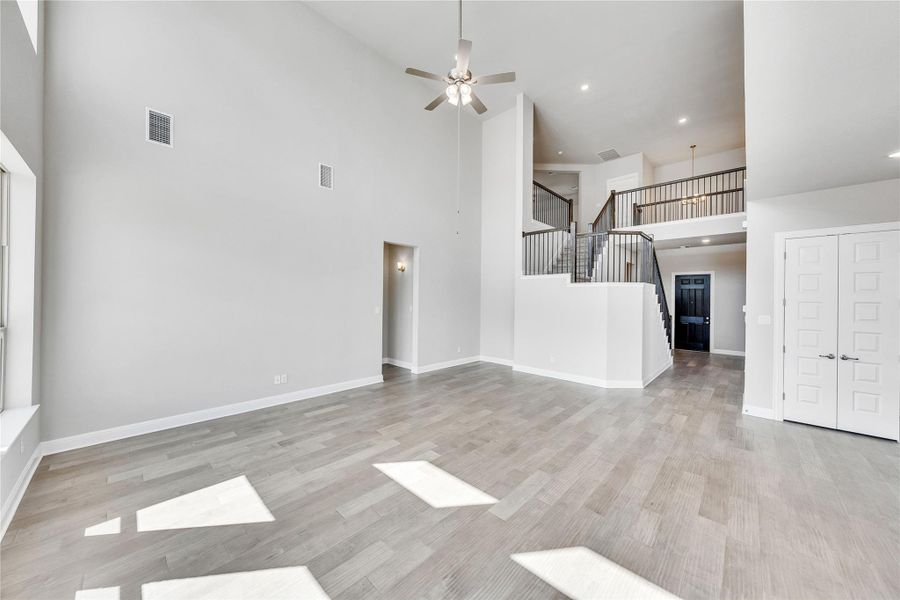 Unfurnished living room featuring a high ceiling, a ceiling fan, recessed lighting, light wood finished floors, and stairs Unfurnished living room featuring a high ceiling, a ceiling fan, recessed lighting, light wood finished floors, and stairs