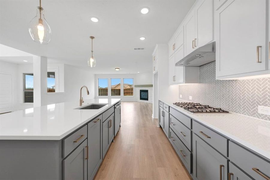 Modern kitchen featuring a large center island with a built-in sink, pendant lighting, two-tone cabinetry, a gas range, and wood-finish flooring