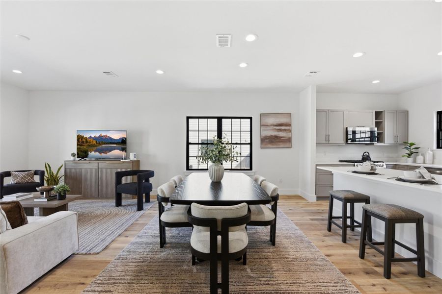 A modern open-concept living area with dining space, hardwood floors, neutral tones, and abundant natural light that creates a bright, welcoming atmosphere.