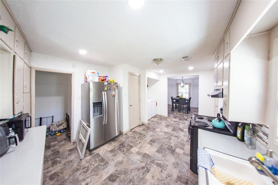 Kitchen with stainless steel fridge, electric range, white cabinets, light countertops, and range hood