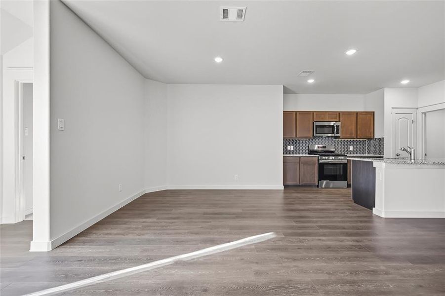 Kitchen featuring brown cabinets, backsplash, appliances with stainless steel finishes, dark wood-style floors, and light stone countertops Kitchen featuring brown cabinets, backsplash, appliances with stainless steel finishes, dark wood-style floors, and light stone countertops