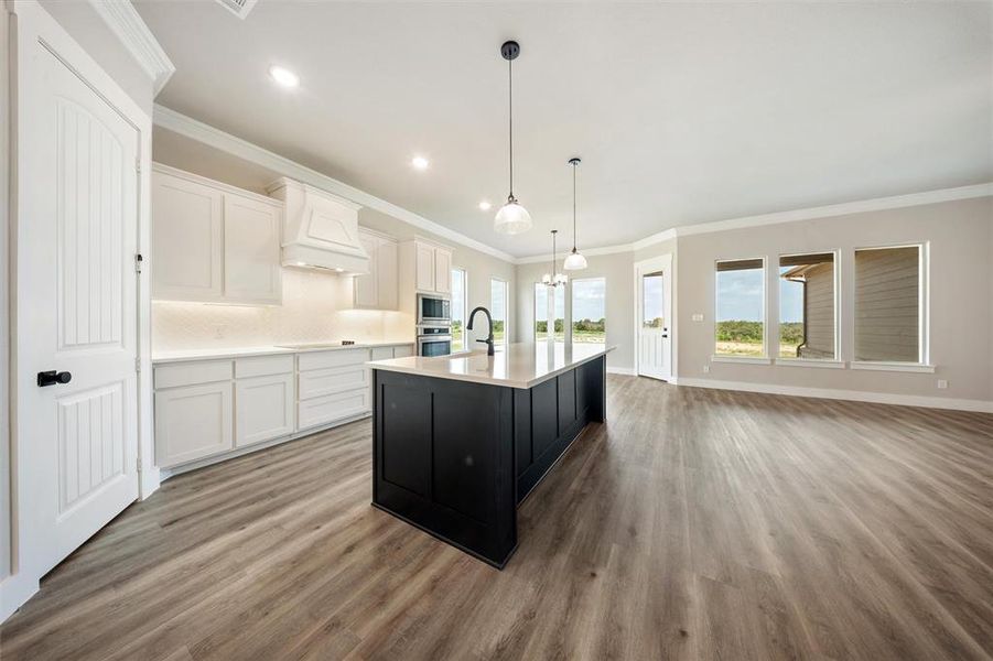 Kitchen with light countertops, wood finished floors, a kitchen island with sink, decorative backsplash, and recessed lighting Kitchen with light countertops, wood finished floors, a kitchen island with sink, decorative backsplash, and recessed lighting
