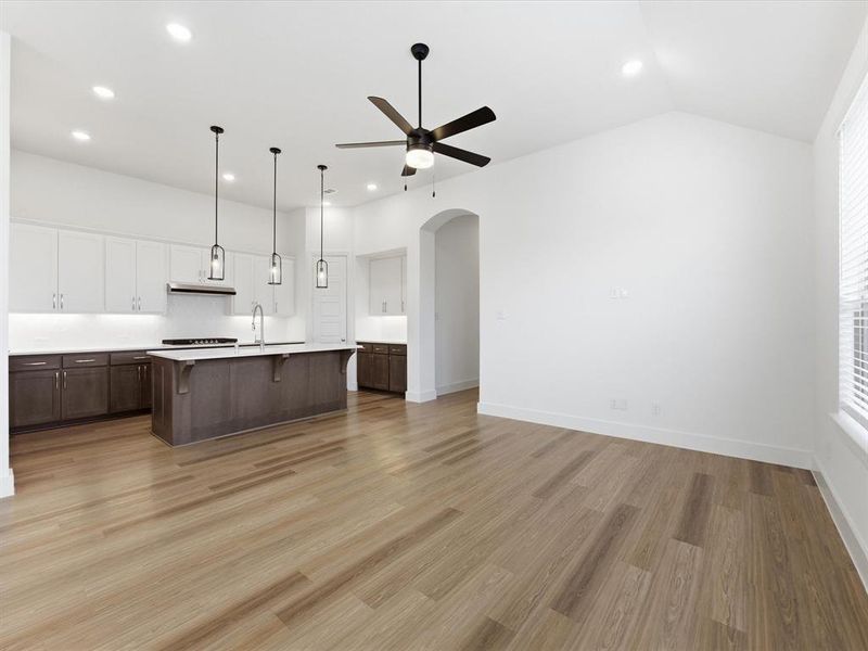 Unfurnished Dining Area featuring open floor plan, a breakfast bar area, a ceiling fan, a center island with sink, and arched walkways