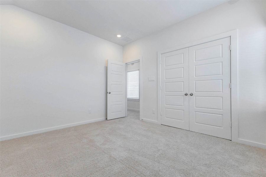 Secondary bedroom with soft carpet, neutral walls, recessed lighting, and double closet doors for generous storage. The simple, bright design makes this room flexible for a guest bedroom, child’s room, home office, hobby space, or quiet study area.