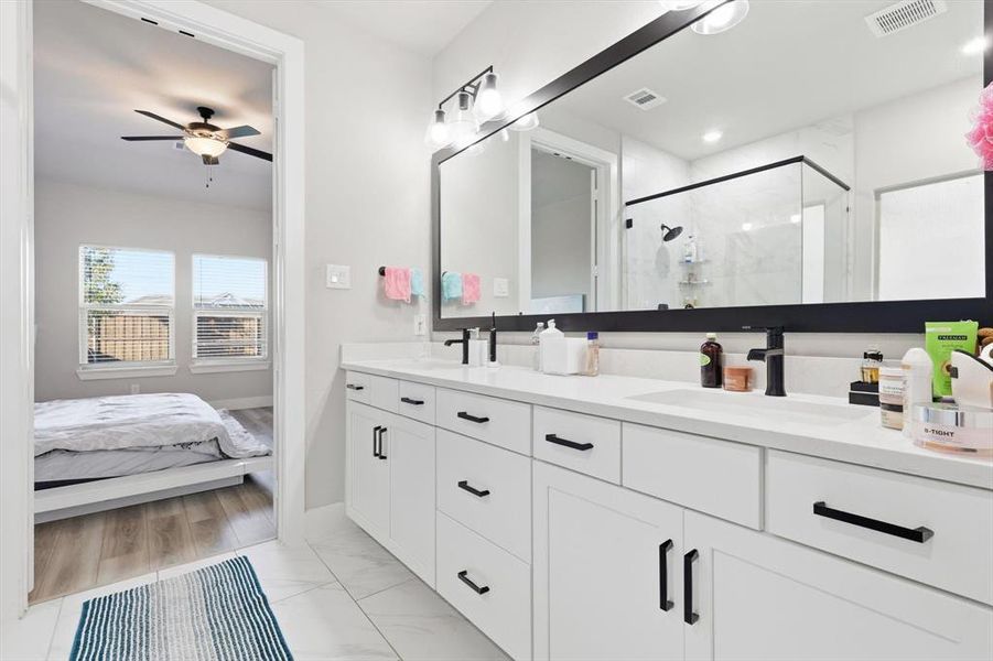 Full bathroom featuring double vanity, a stall shower, ceiling fan, and light marble finish floors