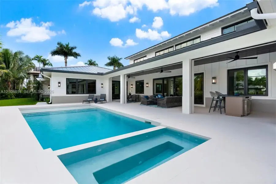 Modern exterior featuring board-and-batten siding, a covered patio with integrated ceiling fans, a built-in outdoor kitchen, and a swimming pool with a built-in spa Modern exterior featuring board-and-batten siding, a covered patio with integrated ceiling fans, a built-in outdoor kitchen, and a swimming pool with a built-in spa