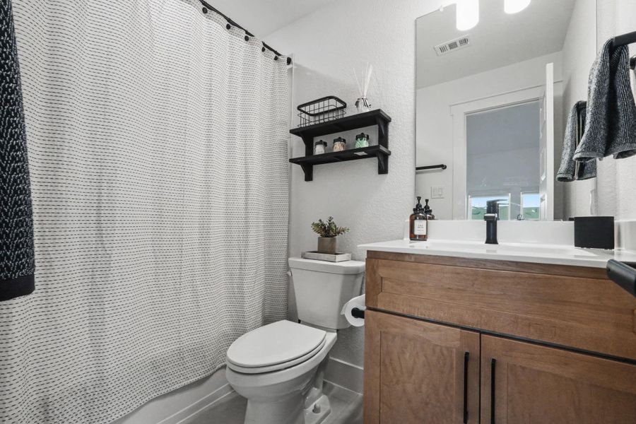 Chic full bath with modern vanity, updated fixtures, and stylish open shelving for added storage and display. Clean, contemporary finishes complete this comfortable and functional space.