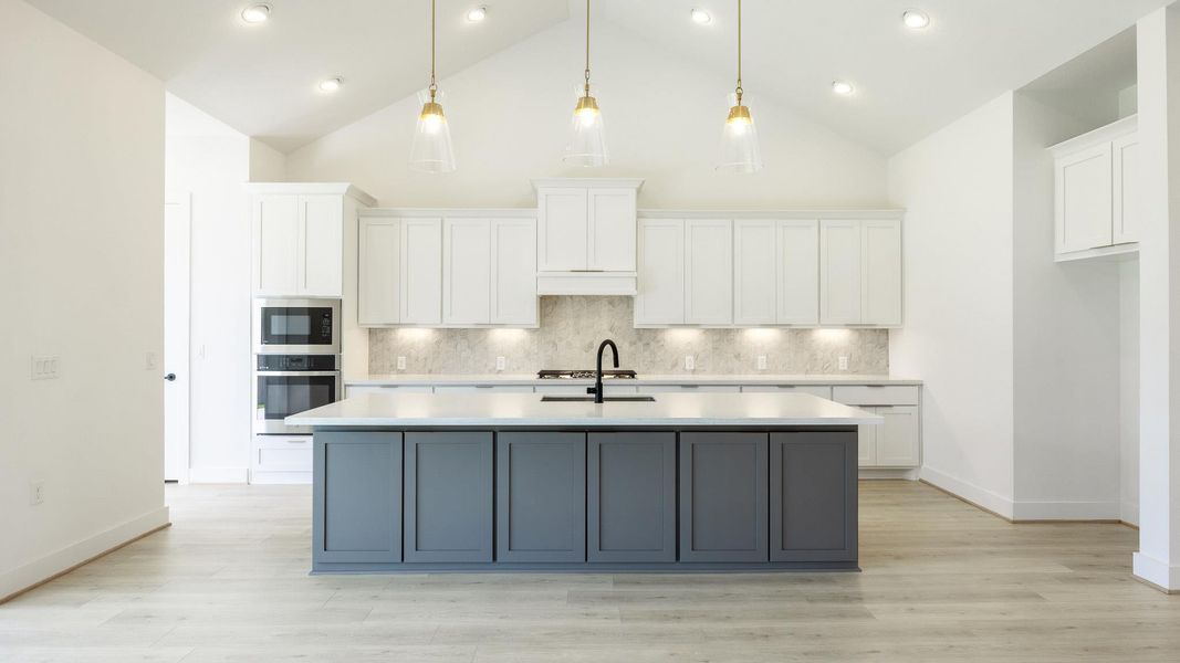 Kitchen with white cabinetry, appliances with stainless steel finishes, backsplash, decorative light fixtures, and high vaulted ceiling Kitchen with white cabinetry, appliances with stainless steel finishes, backsplash, decorative light fixtures, and high vaulted ceiling