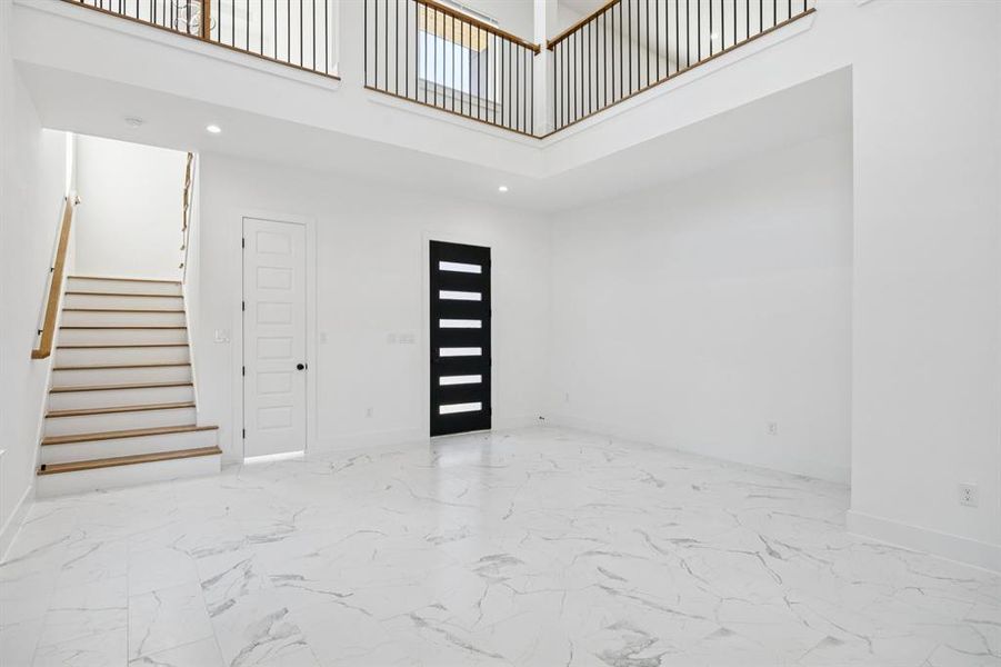 Entrance foyer with a towering ceiling, stairs, recessed lighting, and light marble finish flooring