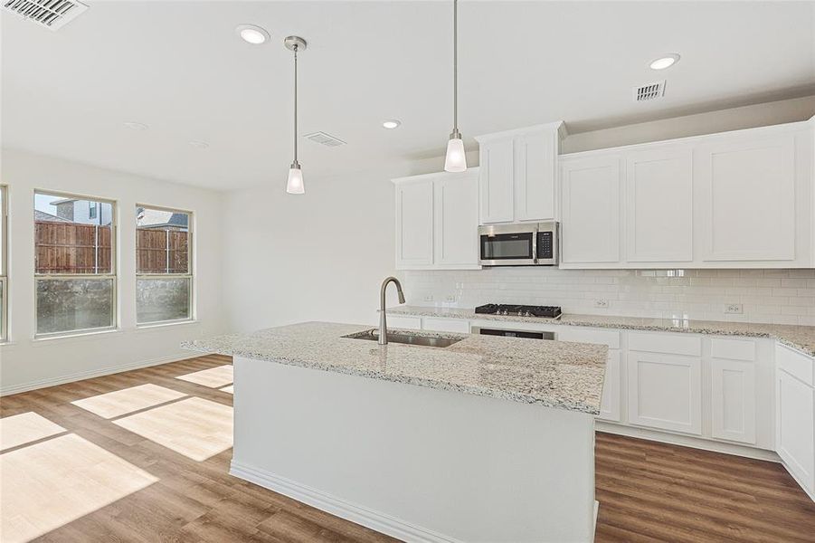 Kitchen with light stone countertops, white cabinets, a kitchen island with sink, wood finished floors, and stainless steel appliances