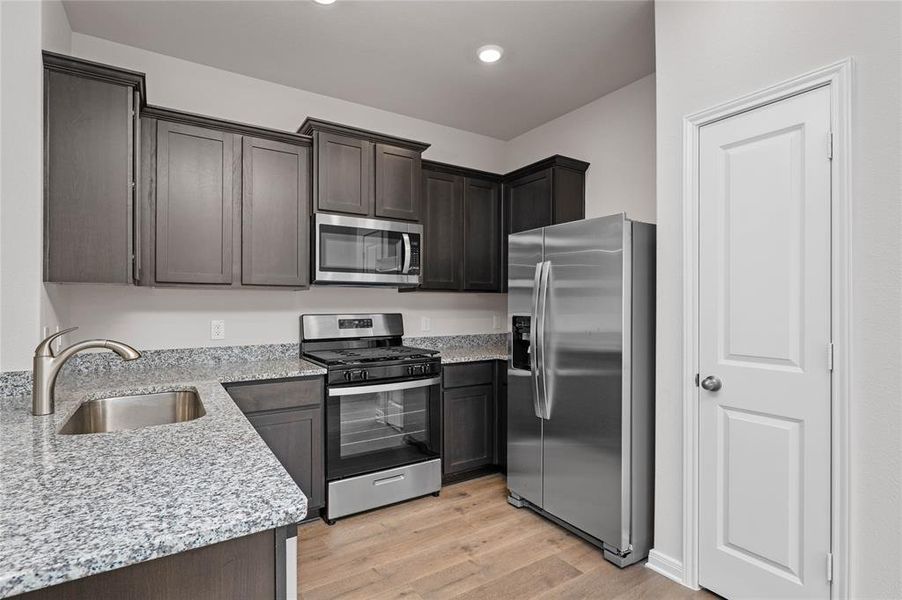 Kitchen featuring appliances with stainless steel finishes, light stone countertops, light wood-style flooring, and dark brown cabinets
