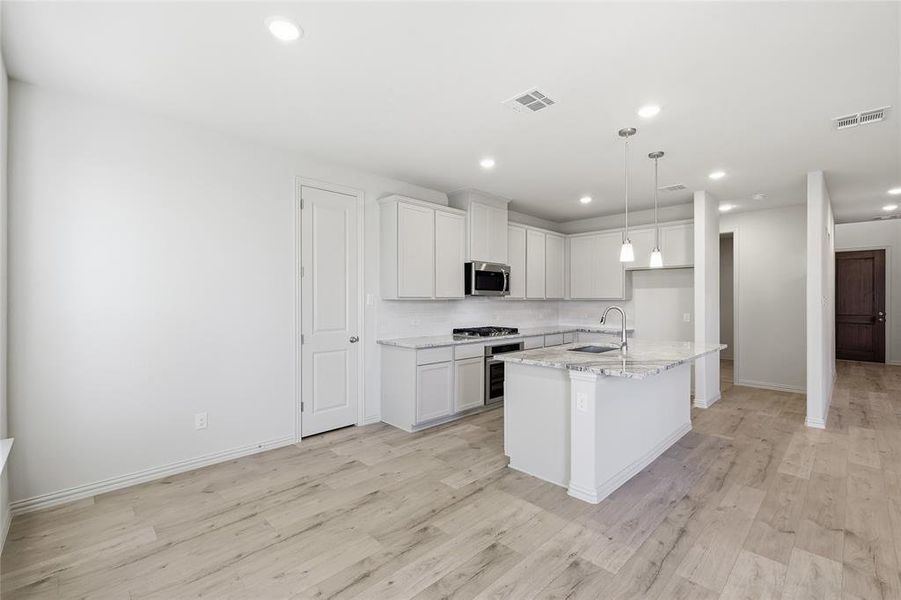 Kitchen with white cabinets, an island with sink, light stone countertops, decorative light fixtures, and light wood-type flooring