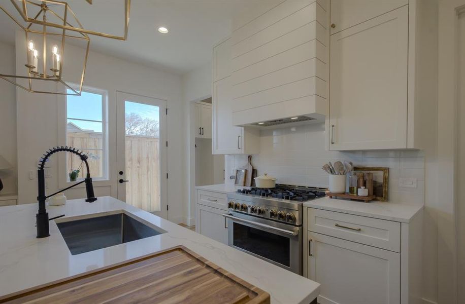 Kitchen with hanging light fixtures, sink, high end stainless steel range, a notable chandelier, and light stone counters