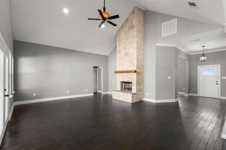 Unfurnished living room with a ceiling fan, dark wood-type flooring, high vaulted ceiling, and a stone fireplace