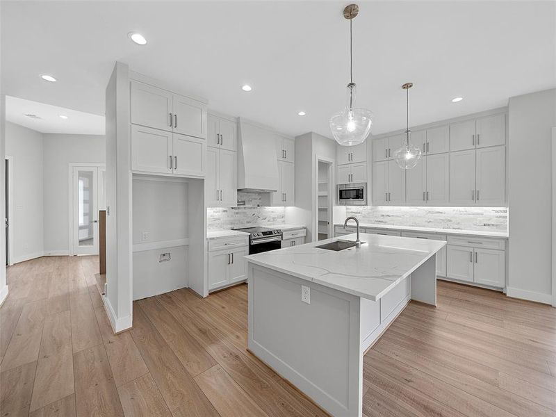 Kitchen with sink, custom range hood, an island with sink, light hardwood / wood-style floors, and stainless steel appliances