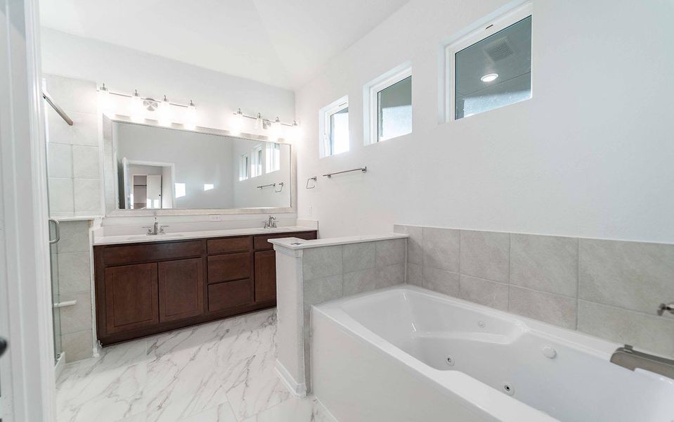 Full bath with a jetted tub, double vanity, light marble finish floors, and a stall shower