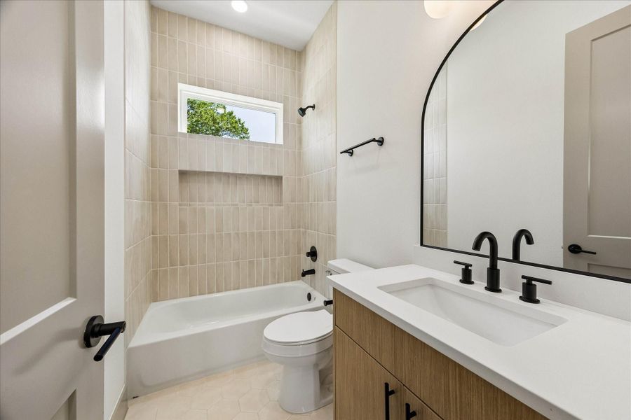 Designer tile, warm wood cabinetry, matte black hardware, and an arched mirror create a bathroom that feels clean, timeless, and elevated.