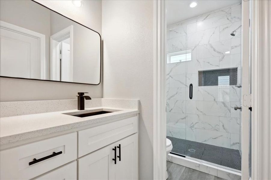 Bathroom featuring a shower with shower door, vanity, wood-type flooring, and toilet