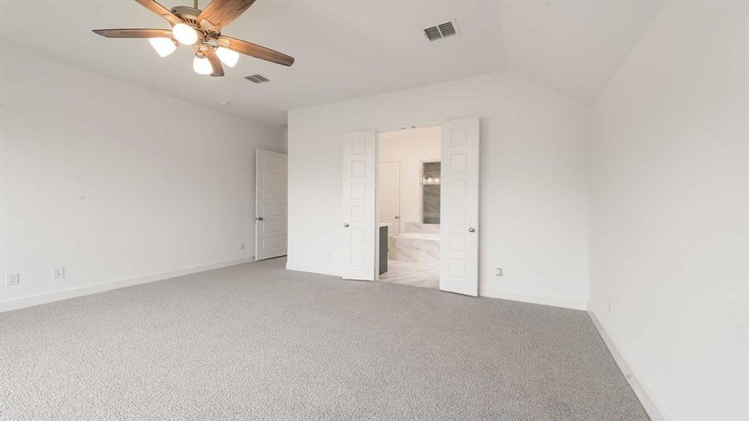 Unfurnished bedroom featuring ceiling fan, ensuite bathroom, light colored carpet, and vaulted ceiling