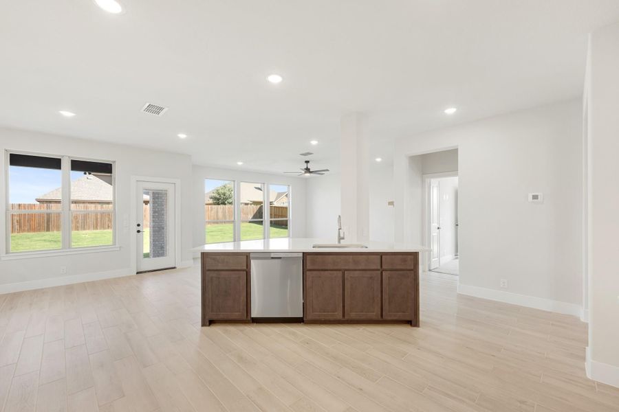 Kitchen island with dark wood cabinets and stainless dishwasher in open-plan living area with light wood floors