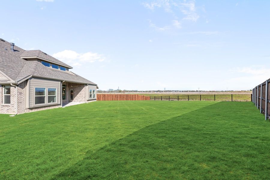 Large backyard with green lawn, black metal fence, and brick home exterior with open field views behind