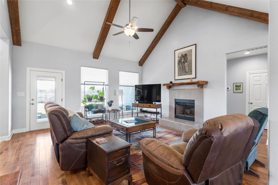 Living area featuring oak- wood- flooring, ceiling fan,  tile fireplace, lofted ceiling, and plenty of natural light