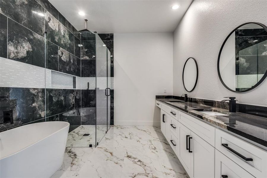 Full bath featuring double vanity, a freestanding tub, a sink, a shower stall, and marble finish floor