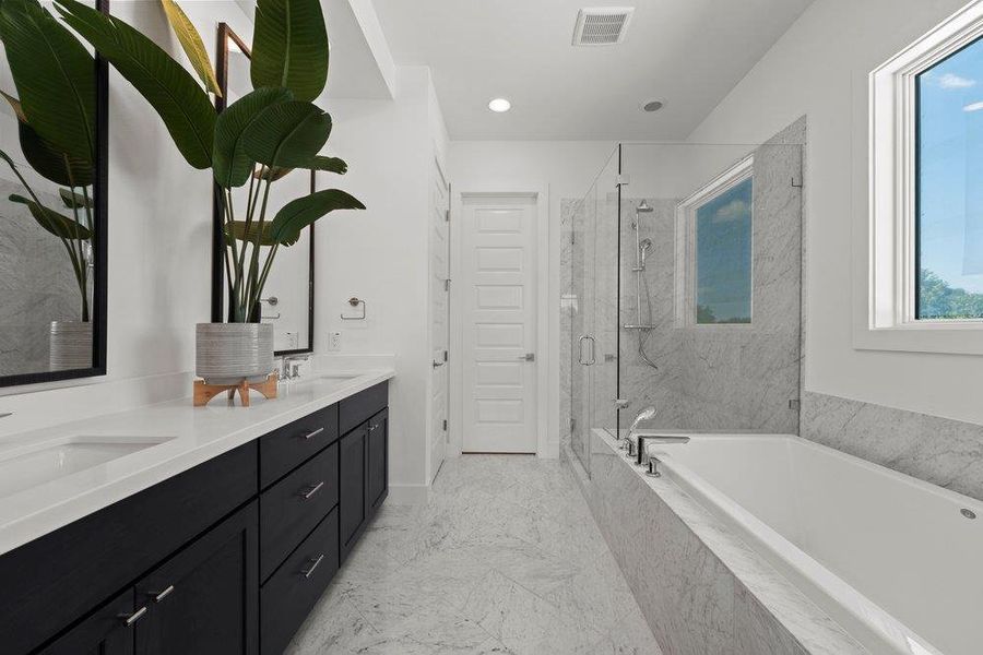Luxurious primary bathroom with dual vanities, oversized soaking tub, frameless glass shower, and elegant carrara marble finishes.