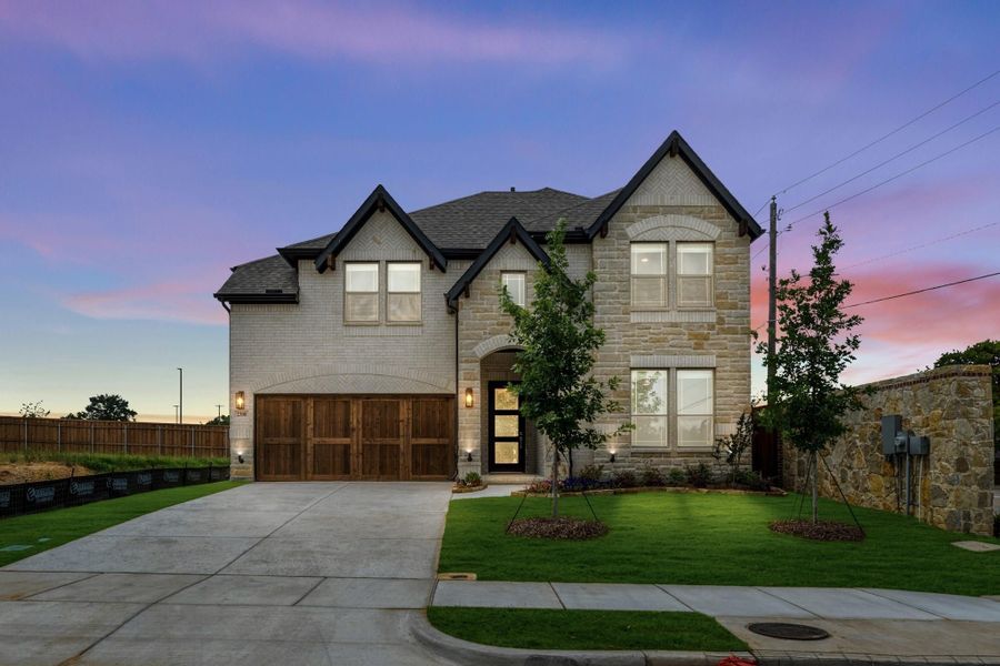 Two-story home with stone and brick exterior, wood garage door, arched entry, and landscaped front yard at dusk