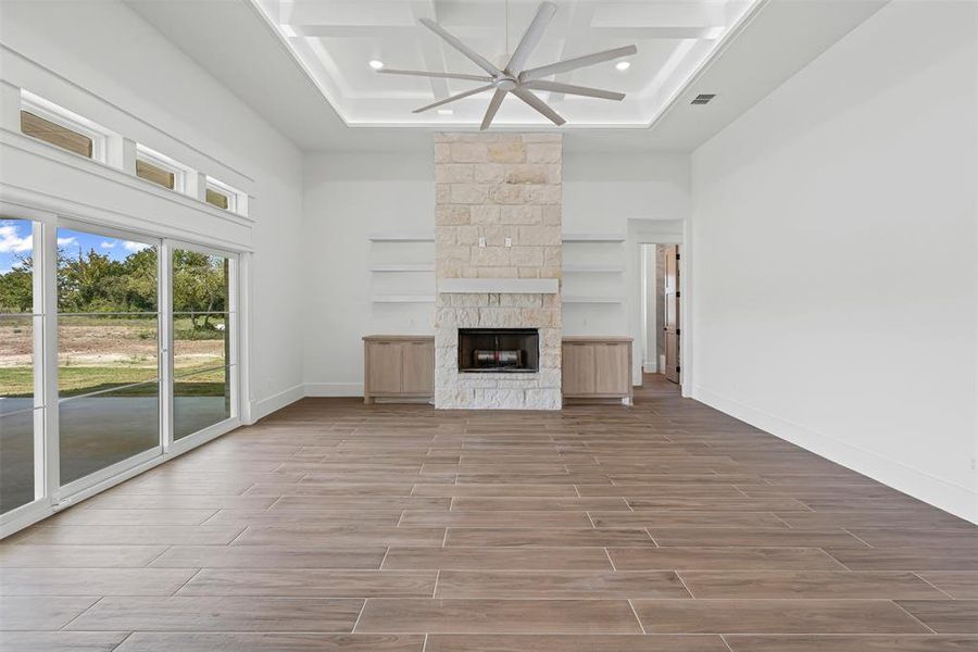 Unfurnished living room with wood finish floors, a stone fireplace, a ceiling fan, a towering ceiling, and coffered ceiling Unfurnished living room with wood finish floors, a stone fireplace, a ceiling fan, a towering ceiling, and coffered ceiling