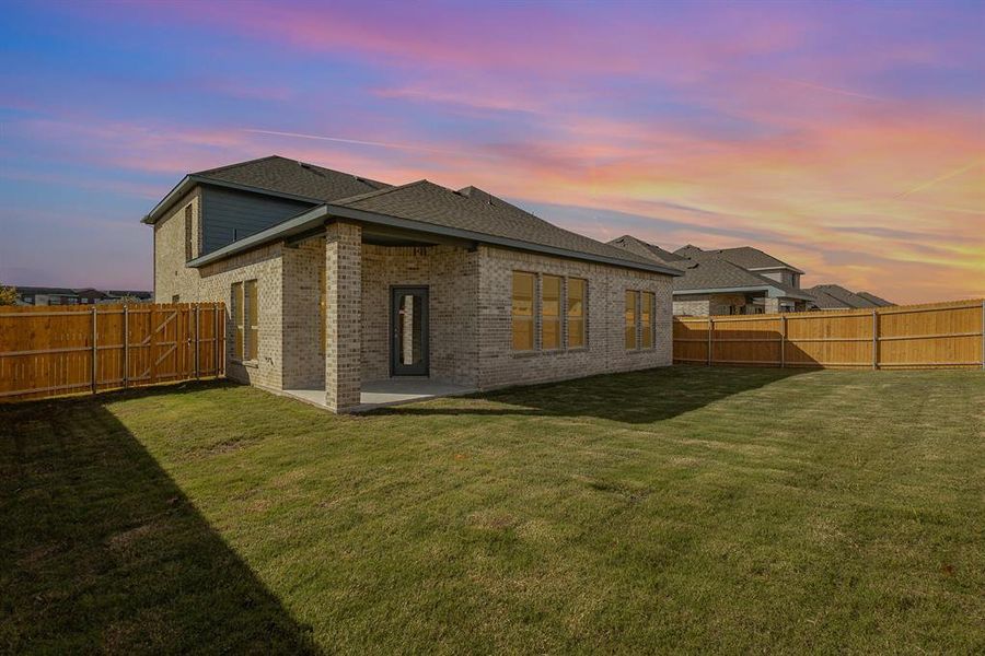 Back house at dusk with a patio area and a lawn