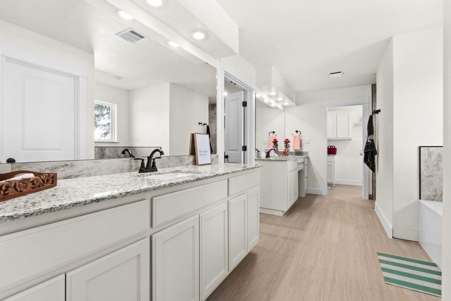 Bathroom with two vanities, light wood-style floors, a tub to relax in, and recessed lighting