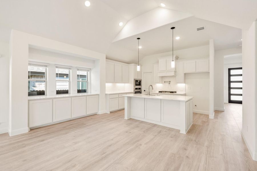 Open kitchen with white cabinets, center island, pendant lights, and light wood floors
