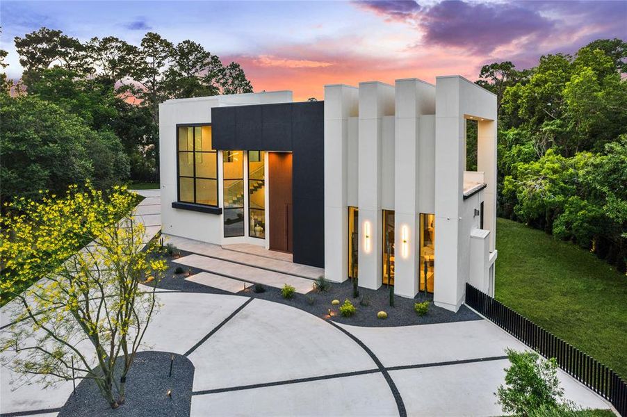 This luxury Piney Point Village estate features a sleek, long concrete driveway that complements its contemporary design while providing ample guest parking. Blackened steel sconces accentuate the exterior, adding a touch of sophistication and elegance to the home's facade.