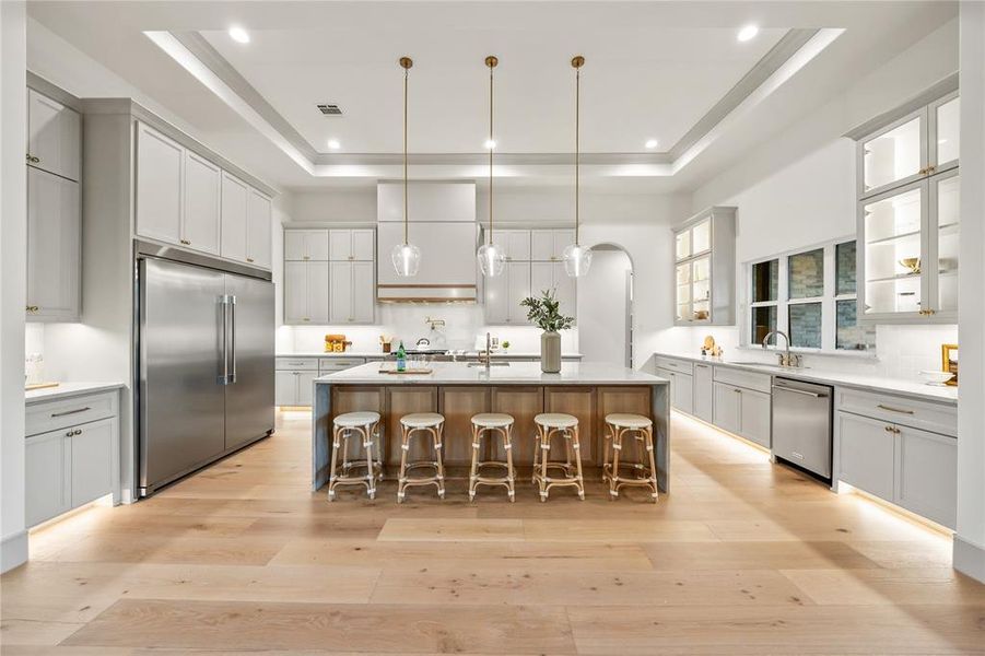Kitchen featuring decorative light fixtures, a center island with sink, stainless steel appliances, light wood finished floors, and a kitchen breakfast bar Kitchen featuring decorative light fixtures, a center island with sink, stainless steel appliances, light wood finished floors, and a kitchen breakfast bar