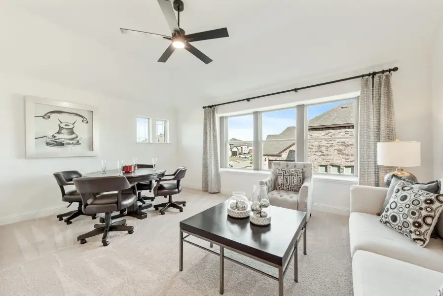 Bright living room with ceiling fan, carpet floors, seating area, and round dining table near large windows