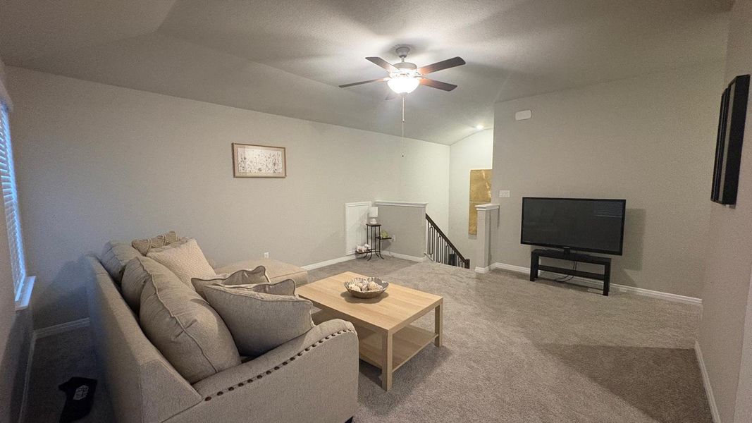 A welcoming upper-level living space with soft carpeting and a ceiling fan for comfort.