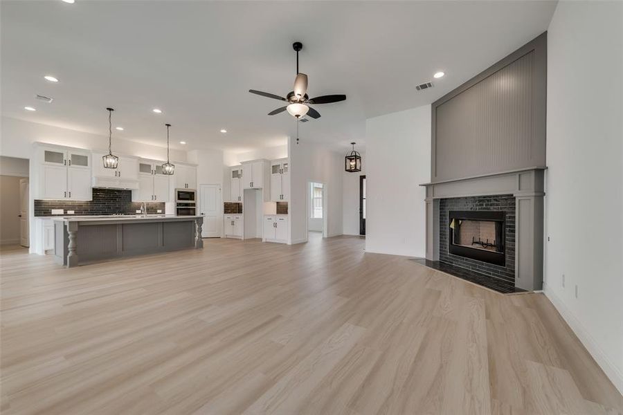 Unfurnished living room with a brick fireplace, sink, ceiling fan, and light wood-type flooring